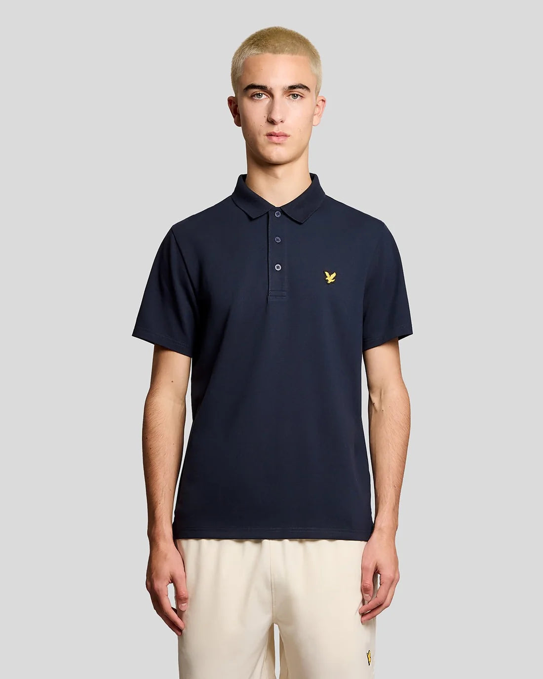 Man wearing a navy polo shirt with a yellow logo on a gray background